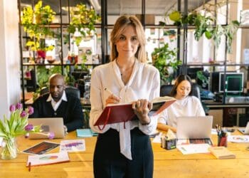 Photo by ANTONI SHKRABA from Pexels: https://www.pexels.com/photo/woman-standing-with-a-notebook-and-people-working-on-laptops-behind-her-in-an-office-7163456/