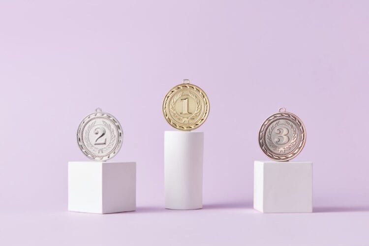 Photo by DS stories: https://www.pexels.com/photo/medals-on-pedestal-on-pink-studio-background-7267588/
