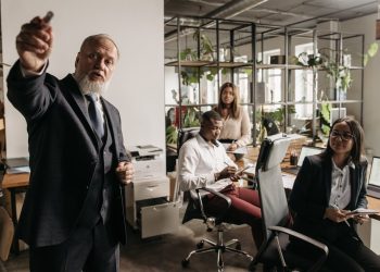 Photo by Pavel Danilyuk from Pexels: https://www.pexels.com/photo/a-man-in-black-suit-talking-beside-people-in-the-office-7654410/