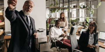 Photo by Pavel Danilyuk from Pexels: https://www.pexels.com/photo/a-man-in-black-suit-talking-beside-people-in-the-office-7654410/