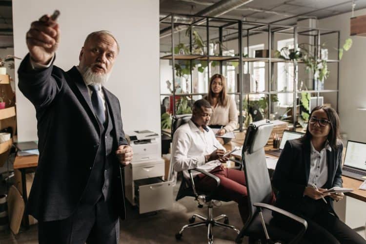 Photo by Pavel Danilyuk from Pexels: https://www.pexels.com/photo/a-man-in-black-suit-talking-beside-people-in-the-office-7654410/