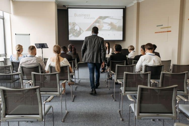 Photo by Pavel Danilyuk from Pexels: https://www.pexels.com/photo/a-man-walking-on-aisle-between-chairs-with-people-sitting-8761317/